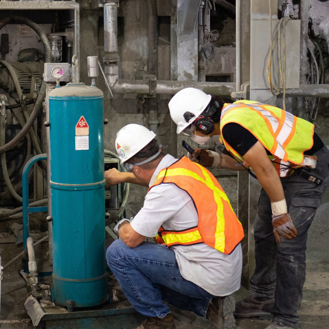 Two men look into an electrical box, blue CJC filter sits in the foreground.